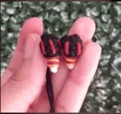 Una Fotografía En Primer Plano De Una Mano Que Sostiene Dos Pequeños Objetos Negros Intrincadamente Tejidos Con Detalles En Rojo Y Naranja Que Se Asemejan a Piezas De Cestería O Abalorios En Miniatura Evocan El Encanto De Los Pequeños Diseños De Amigurumi El Fondo Es Un Verdor Borroso