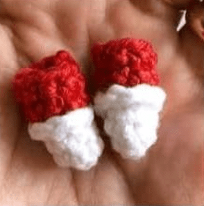 Un Par De Pequeñas Botas De Crochet Cada Una Con Una Parte Superior Roja Y Una Parte Inferior Blanca Descansa Sobre La Palma De Una Persona Estas Botas Amigurumi En Español Son En Miniatura Y Parecen Estar Hechas a Mano