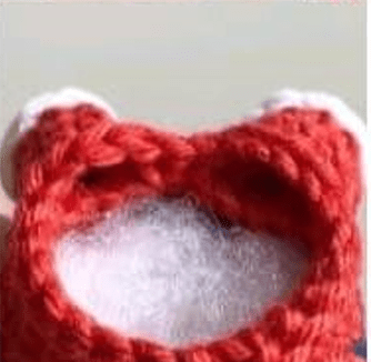 Imagen De Primer Plano De Un Objeto De Ganchillo Rojo Sin Terminar Con Relleno Blanco Visible a Través De Una Abertura En La Parte Superior La Forma Y Apariencia Del Objeto Sugieren Que Podría Ser Parte De Un Juguete O Una Pieza De Peluche Amigurumi En Español