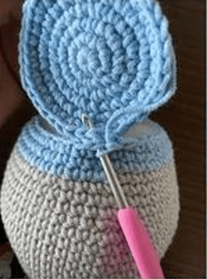 Primer Plano De Un Proyecto De Crochet En Curso Un Ganchillo Con Mango Rosa Está Trabajando Para Unir Un Círculo De Crochet Azul Claro a Una Pieza De Crochet Beige Más Grande Las Piezas Siguiendo Un Patrón Amigurumi En Español Se Cosen Con Prolijos Patrones En Espiral