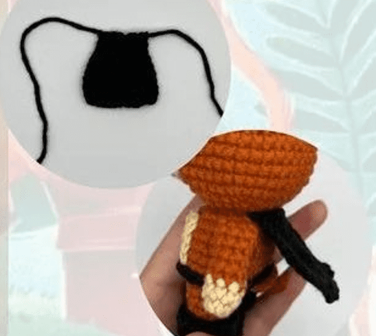 Una Mano Que Sostiene Un Pequeño Zorro Naranja Tejido a Crochet Con Cola Negra Y Patas Blancas Visto Desde Atrás El Recuadro De Arriba Muestra Una Pieza De Crochet Negra Con Forma De Pequeño Rectángulo Con Dos Hilos Que Se Extienden Desde Sus Esquinas Superiores Ideal Para Quienes Buscan Un Patrón Amigurumi Gratis Para Crear Sus Propias Criaturas Encantadoras