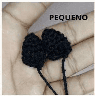 Una Mano Que Sostiene Dos Pequeñas Piezas De Crochet Negras Sobre Un Fondo Claro Con La Palabra pequeno pequeño En Portugués Escrita Encima De Ellas La Pieza De La Izquierda Se Parece Al Amigurumi Goku De Dragon Ball Elaborada Con Intrincados Detalles