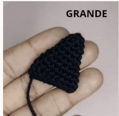 Una Mano Sostiene Un Pequeño Objeto Triangular De Ganchillo Negro Sobre Un Fondo Claro Encima Del Objeto Está Escrito El Texto grande Que Recuerda a Un Intrincado Diseño De Patrón Amigurumi