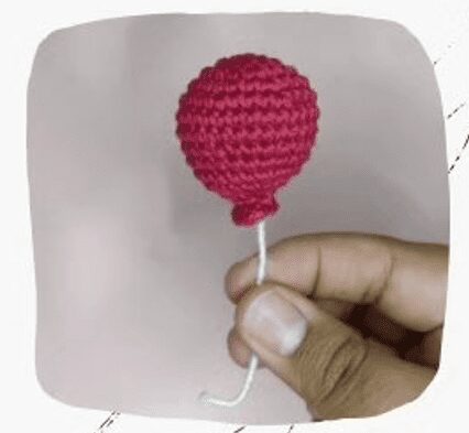 Una Mano Que Sostiene Un Pequeño Globo Tejido De Color Rojo Con Una Cuerda Blanca Atada En La Parte Inferior Sobre Un Fondo Liso De Color Claro