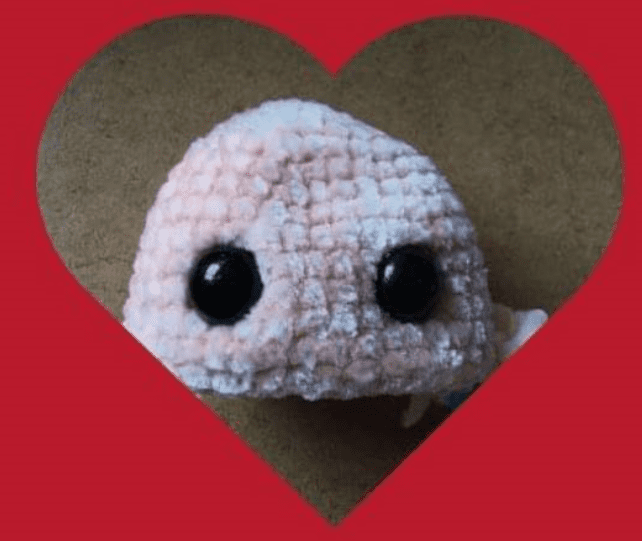 Un Peluche De Ganchillo Con Grandes Ojos Negros Está Enmarcado Dentro De Una Forma De Corazón Rojo El Juguete Tiene Una Textura Suave Y Redonda Y Es Principalmente Blanco Con Algunas Manchas De Color Marrón Claro Está Colocado Sobre Un Fondo Liso