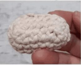 Una Mano Sostiene Un Pequeño Objeto Ovalado Tejido a Crochet Con Hilo Beige El Fondo Es Una Superficie Clara Y Borrosa
