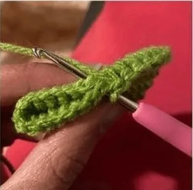 🩷 Cómo Tejer un Amigurumi de Alíen de Toy Story: Patrón Gratis en español 👽 - Primer plano de una persona tejiendo con un ganchillo de mango rosa e hilo verde. El trabajo de crochet está parcialmente terminado y se ven claramente los puntos y la textura del hilo. Relleno de fibra blanca para amigurumis sobre una base tejida, rodeado por ovillos de lana pastel, botones y herramientas de costura.