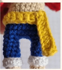 Una Figura Tejida a Crochet Que Lleva Pantalones Azules Zapatos Blancos Y Una Chaqueta Amarilla La Imagen Muestra Una Vista Parcial Centrándose En La Parte Inferior Del Cuerpo Y Capturando Los Intrincados Detalles Del Trabajo De Crochet