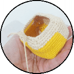 Una Mano Que Sostiene Una Pequeña Cesta Cuadrada De Crochet Con Lados Beige Y Amarillo La Cesta Está Parcialmente Terminada Mostrando Algunos Hilos Sueltos El Fondo Es De Un Color Liso Y Claro