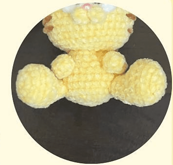 Un Osito De Peluche Amarillo Tejido a Crochet Con La Cabeza Los Brazos Y El Torso Parcialmente Visibles Se Encuentra Centrado Dentro De Un Marco Circular Sobre Un Fondo Oscuro El Osito De Peluche Hecho a Mano Parece Suave Y Lujoso Con Un Diseño Detallado Y Texturizado