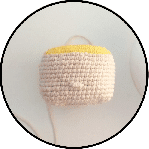 Una Pequeña Pieza De Crochet Beige Hecha a Mano Con Una Parte Superior Amarilla Que Se Asemeja a Un Proyecto Parcialmente Terminado Tiene Una Cola De Hilo Que Se Extiende Desde Allí Lo Que Sugiere Que Todavía Está En Progreso El Fondo Es Una Superficie Lisa Y Clara