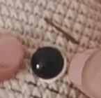 Un Primer Plano De Dos Dedos Sosteniendo Un Pequeño Objeto Esférico Blanco Y Negro Sobre Un Fondo Beige Texturizado