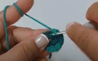 Primer Plano De Una Persona Tejiendo a Crochet Con Hilo Verde Azulado Sus Manos Sostienen Un Ganchillo Y Trabajan En Una Pequeña Pieza Circular La Persona Tiene Esmalte De Uñas De Color Claro