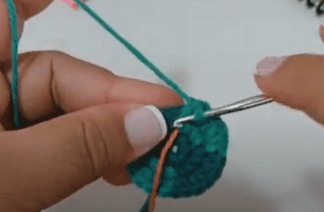 Primer Plano De Unas Manos Tejiendo a Crochet Con Hilo Turquesa Las Manos Sostienen Una Pieza De Crochet Redonda Parcialmente Terminada Y Se Inserta Un Ganchillo En Los Puntos Las Uñas De La Persona Están Pintadas De Rosa Claro También Se Ve Otro Trozo De Hilo Posiblemente Un Marcador De Puntos