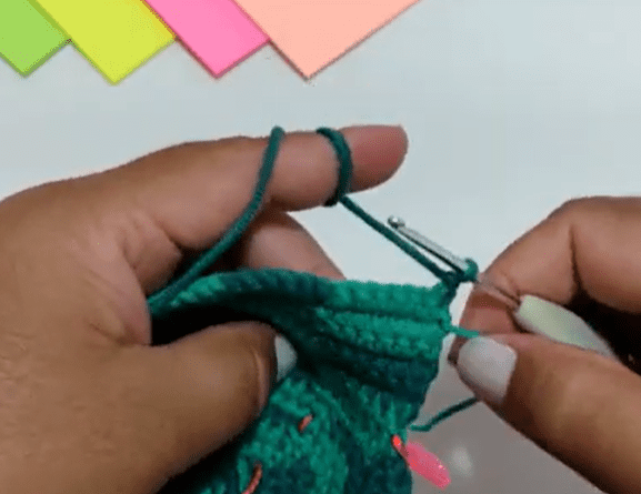 Primer Plano De Unas Manos Tejiendo Con Un Hilo Verde Y Una Aguja De Crochet Se Pueden Ver Notas Adhesivas De Colores En El Fondo La Persona Parece Estar Tejiendo Una Pieza De Crochet Verde