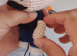 Manos cosiendo una camisa amigurumi de Don Ramón tejida a crochet.