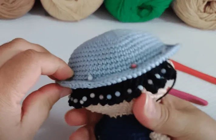 Manos uniendo un gorro tejido a crochet a una figura amigurumi de Don Ramón.