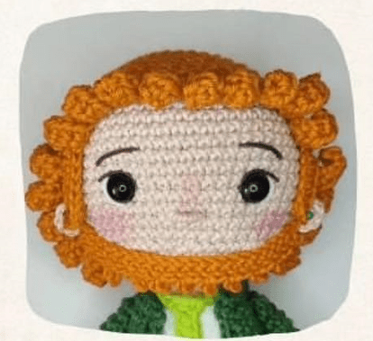 Un Muñeco Amigurumi Tejido a Crochet Con Pelo Rizado De Color Naranja Ojos Negros Y Cara De Color Claro Lleva Un Traje Verde Con Una Pequeña Bufanda Blanca Y Verde Claro El Fondo Es Liso Y De Color Claro Perfecto Para Mostrar La Creación Gratuita De Este Patrón