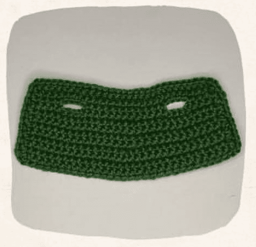 Pieza De Tejido De Crochet Verde De Forma Rectangular Con Bordes Redondeados Y Con Dos Aberturas Horizontales Cerca De La Parte Superior Creada Con Un Patrón Gratuito La Tela Se Muestra Sobre Un Fondo Liso Y De Color Claro