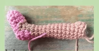 Una Pieza De Crochet Con Forma De Hueso O Tubo De Color Marrón Claro Con Un Extremo Redondeado De Color Rosa Que Recuerda a Algo Que Mirabel Madrigal Podría Crear Yace Plana Sobre Una Superficie De Madera El Trabajo De Crochet Parece Estar En Progreso Con Algunos Hilos De Hilo Colgantes Visibles