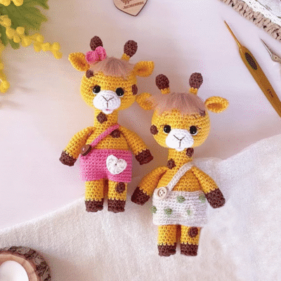 Adorables juguetes amigurumi de jirafa tejidos a crochet, uno en color rosa y otro con traje verde.