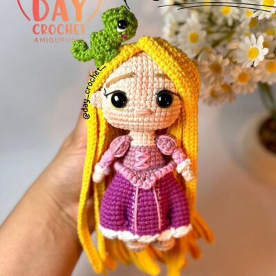 Muñeca De Amigurumi De Rapunzel Con Cabello Amarillo Y Vestido Rosa Y Morado Sosteniendo Un Pequeño Personaje Verde