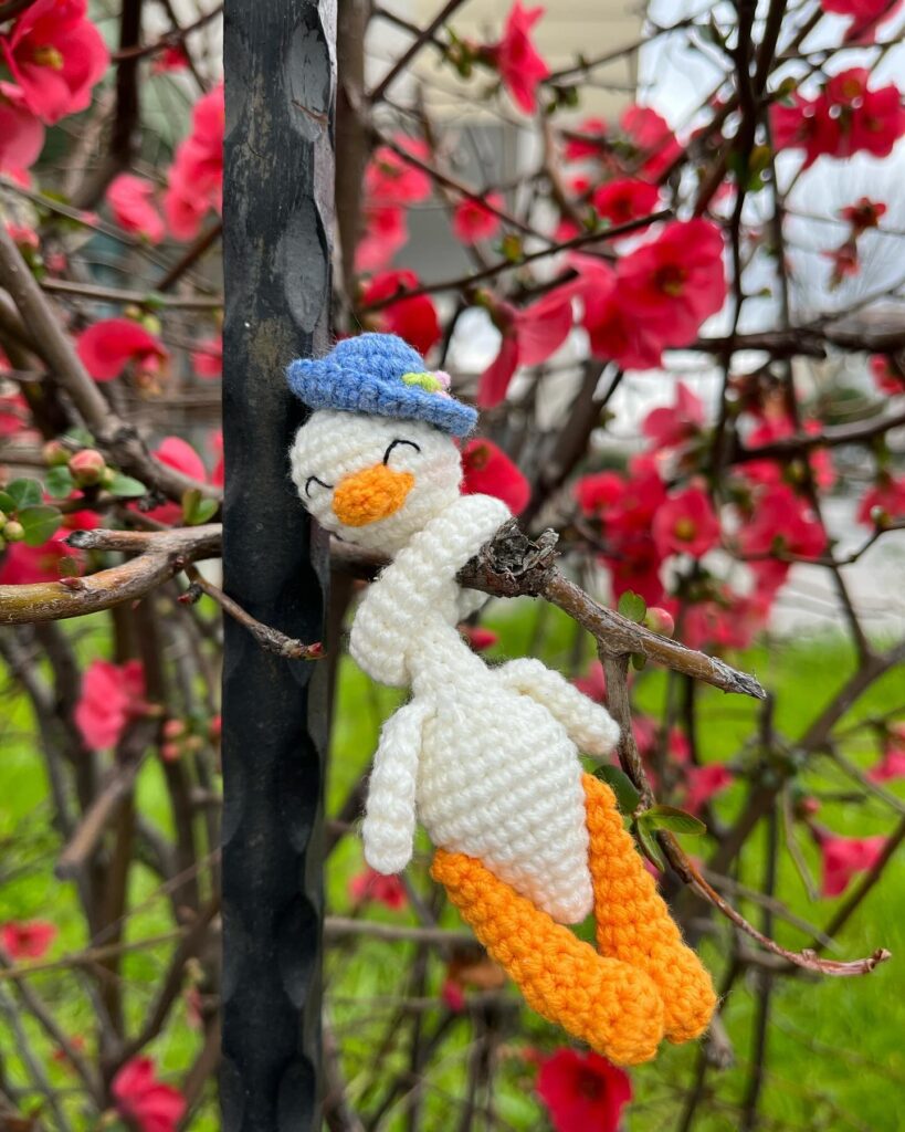 Adorable Pato Amigurumi Tejido a Crochet Con Sombrero Posado En Una Rama En Flor