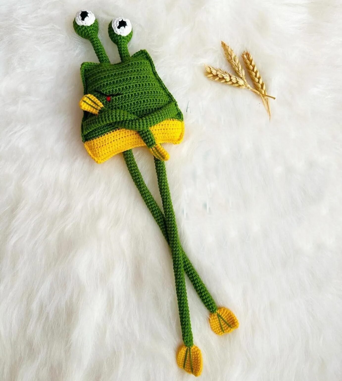 Rana amigurumi verde con ojos grandes y patas extensibles, tejida a crochet sobre una superficie de madera, mostrando su divertido diseño.