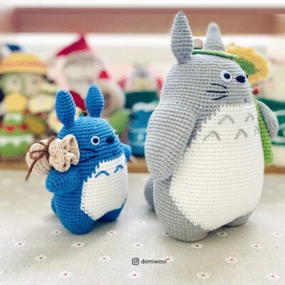 Adorables Peluches De Totoro Tejidos a Crochet Uno Azul Y Otro Gris Expuestos Sobre Una Tela Floral